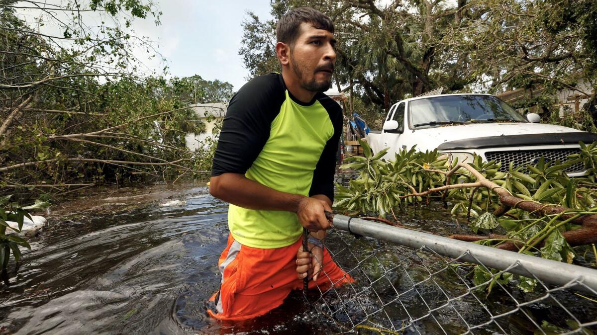 Israel Alvarado, 25, tries to open a gate blocked by fallen tree branches so that he can retrieve a generator in Bonita Springs, Fla.