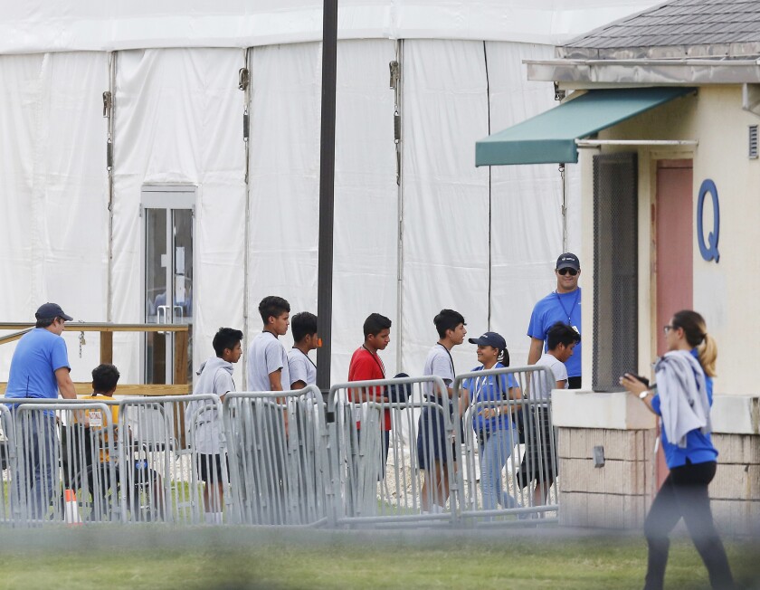 Immigrant children walk in a line outside a shelter