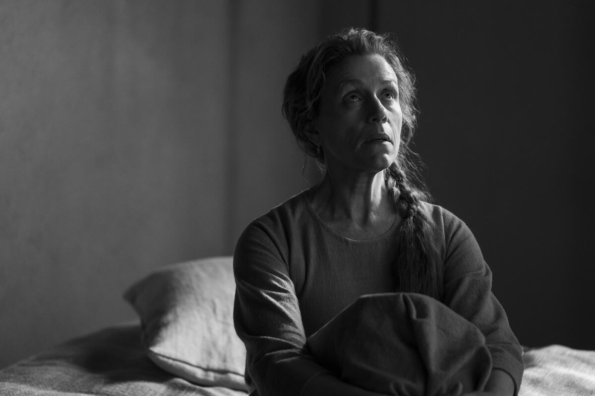 A woman sits on a bed, looking upward.