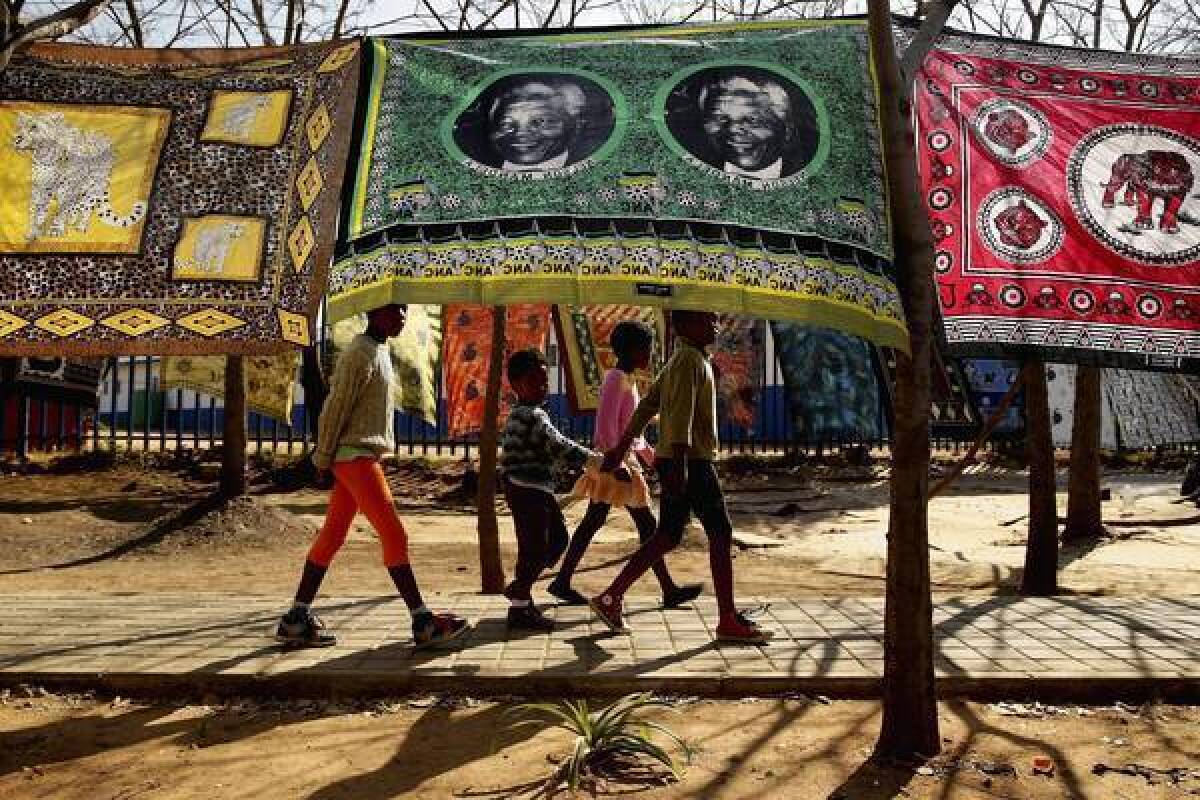 Children in Johannesburg, South Africa, pass by a souvenir flag of former President Nelson Mandela. Mandela, 94, is hospitalized in critical condition, and President Obama will defer to his family on whether he should pay a visit during his Africa tour.