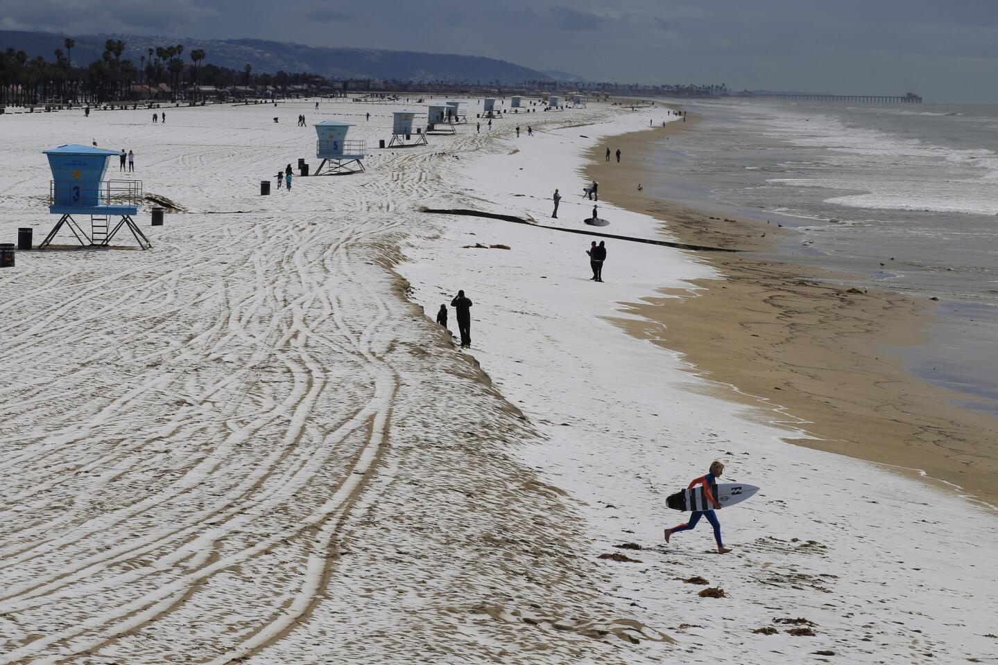 A surfer runs across the hail-covered sand in Huntington Beach.