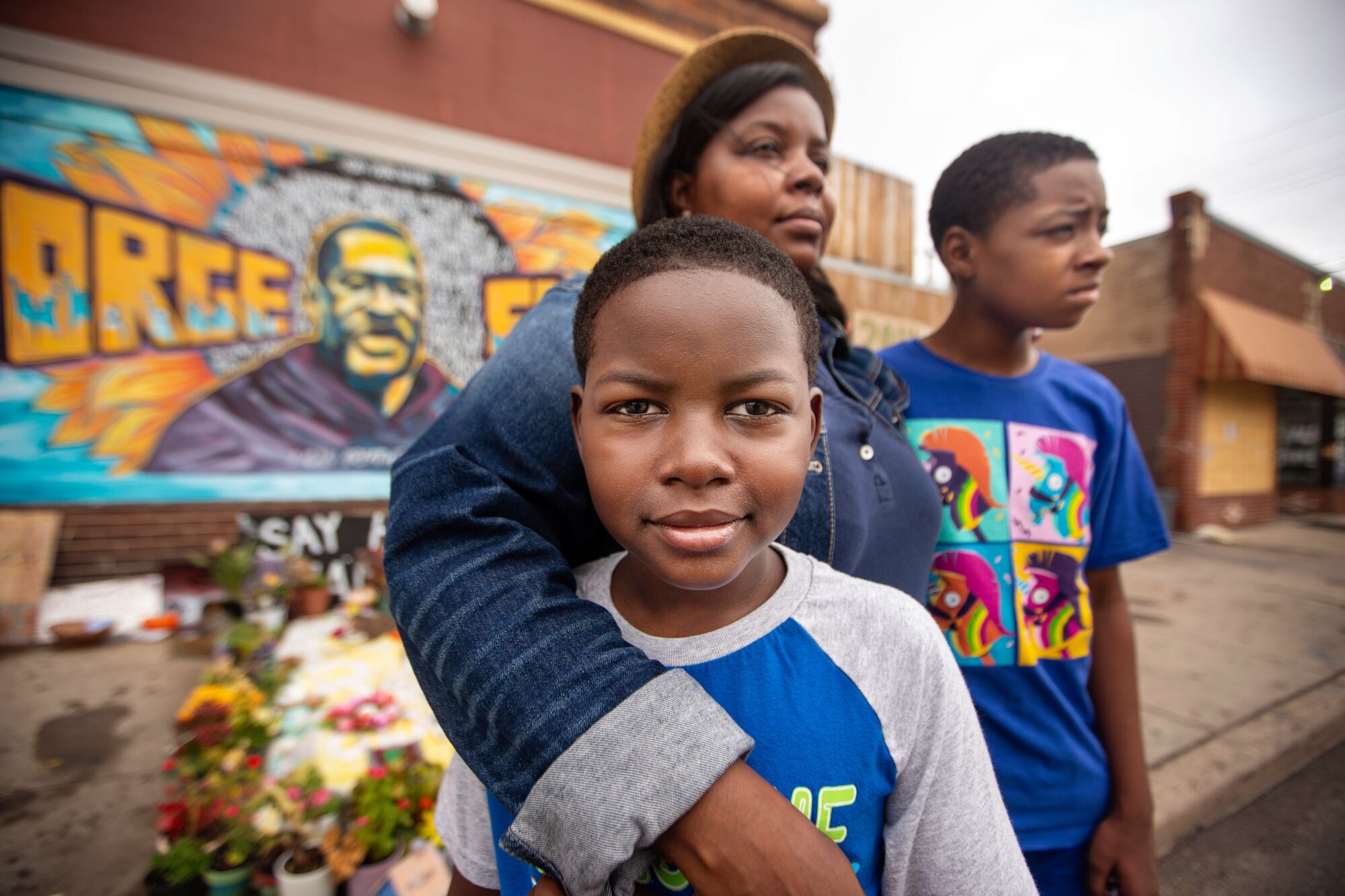Alonzo Smith stands with his mother, Alicia, and brother, Walter III, in front of a George Floyd mural in Minneapolis.