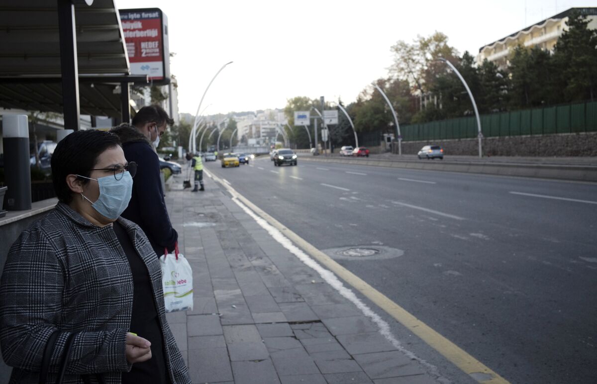 People wearing masks to help protect against the spread of coronavirus, wait at a bus station, in Ankara, Turkey, Wednesday, Nov. 11, 2020. Turkey's government had urged the residents of big cities to limit their mobility and called on employers to offer workers flexible or staggered working hours and the possibility of working from homes.(AP Photo/Burhan Ozbilici)