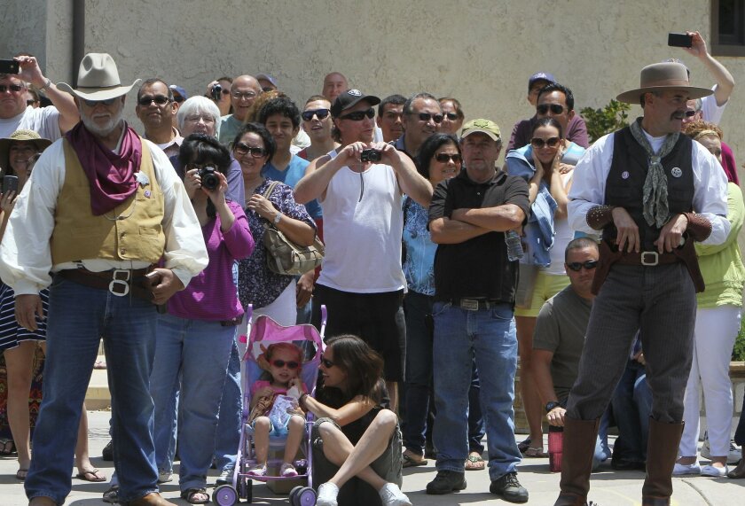 With cowboys on either side of them, spectators take photographs of a "bank robbery" in Old Town Temecula during the annual Western Days event Saturday.