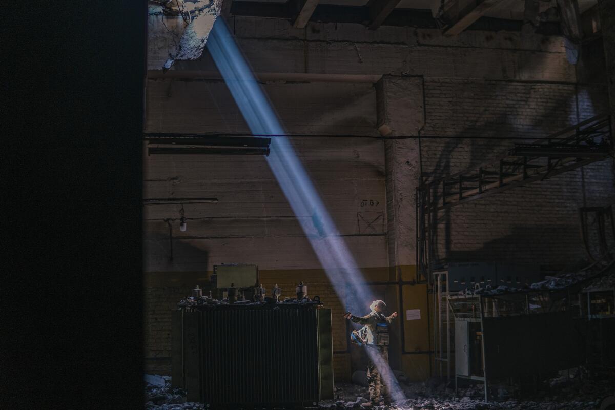 A Ukrainian soldier inside the ruined Azovstal steel plant stands in a ray of sunlight.