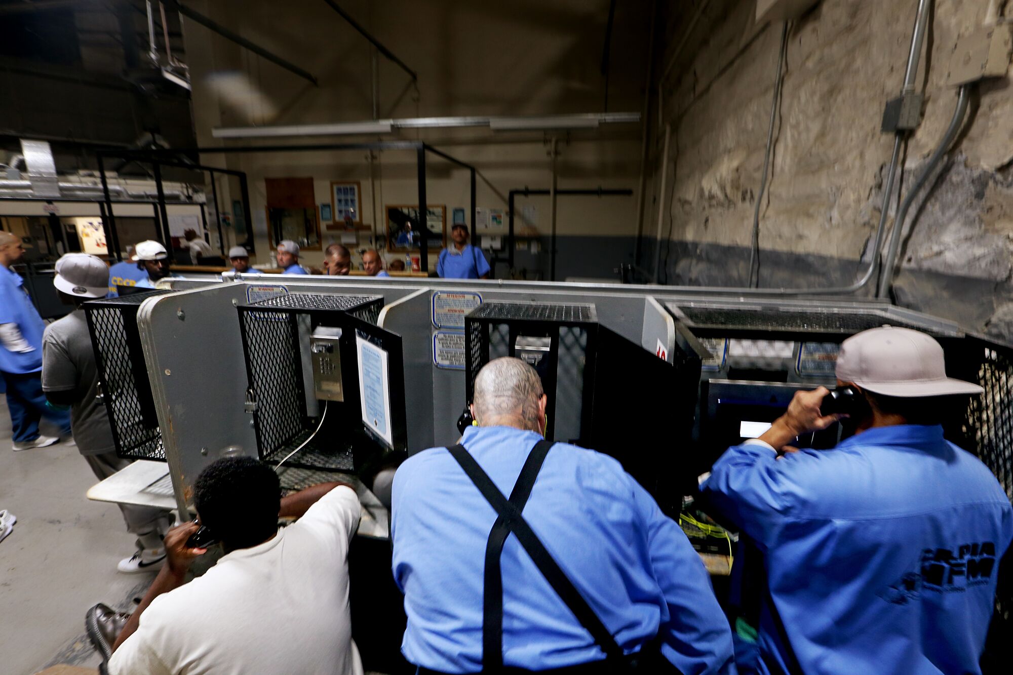 Men talking on the phone in side-by-side cubicles as other men stand by