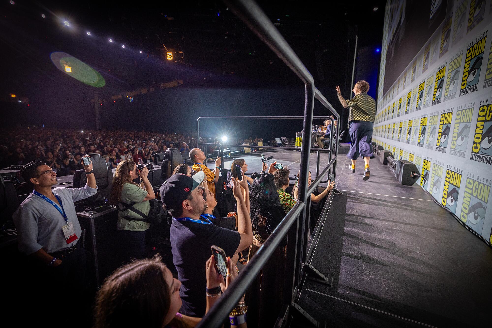 A woman walks up on stage and waves to a cheering crowd.