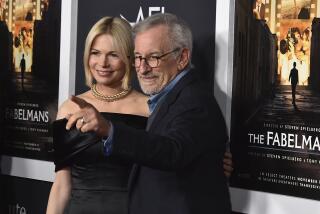A blond woman in a black dress and a man with gray hair and glasses who is pointing in a black suit