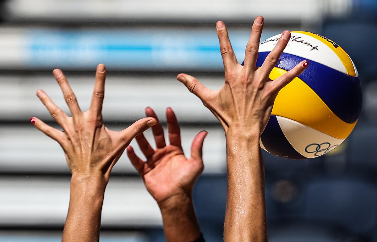 Two beach volleyball players raise their hands above the net toward the ball.