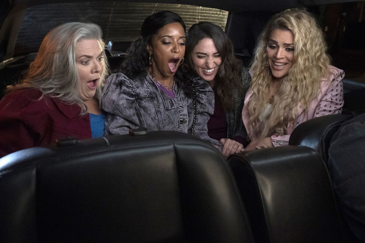 Four women looking shocked at something in the back of a limousine