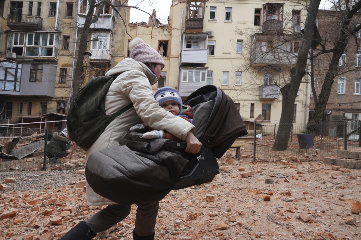 A woman hurries across a rubble-strewn lot with a baby in a carrier.