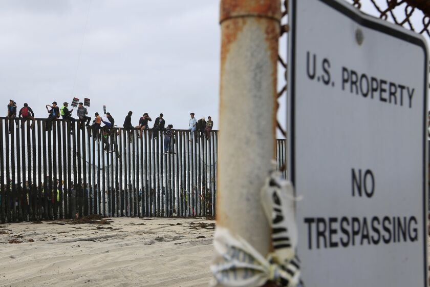 Central American migrants and their supporters sat on top of the border wall during a rally in support of the migrants on Sunday, April 29, 2018. Groups on both sides of the border gathered at Border Field State Park before the asylum seekers planned to try to enter the United States. (Photo by K.C. Alfred/ San Diego Union -Tribune)