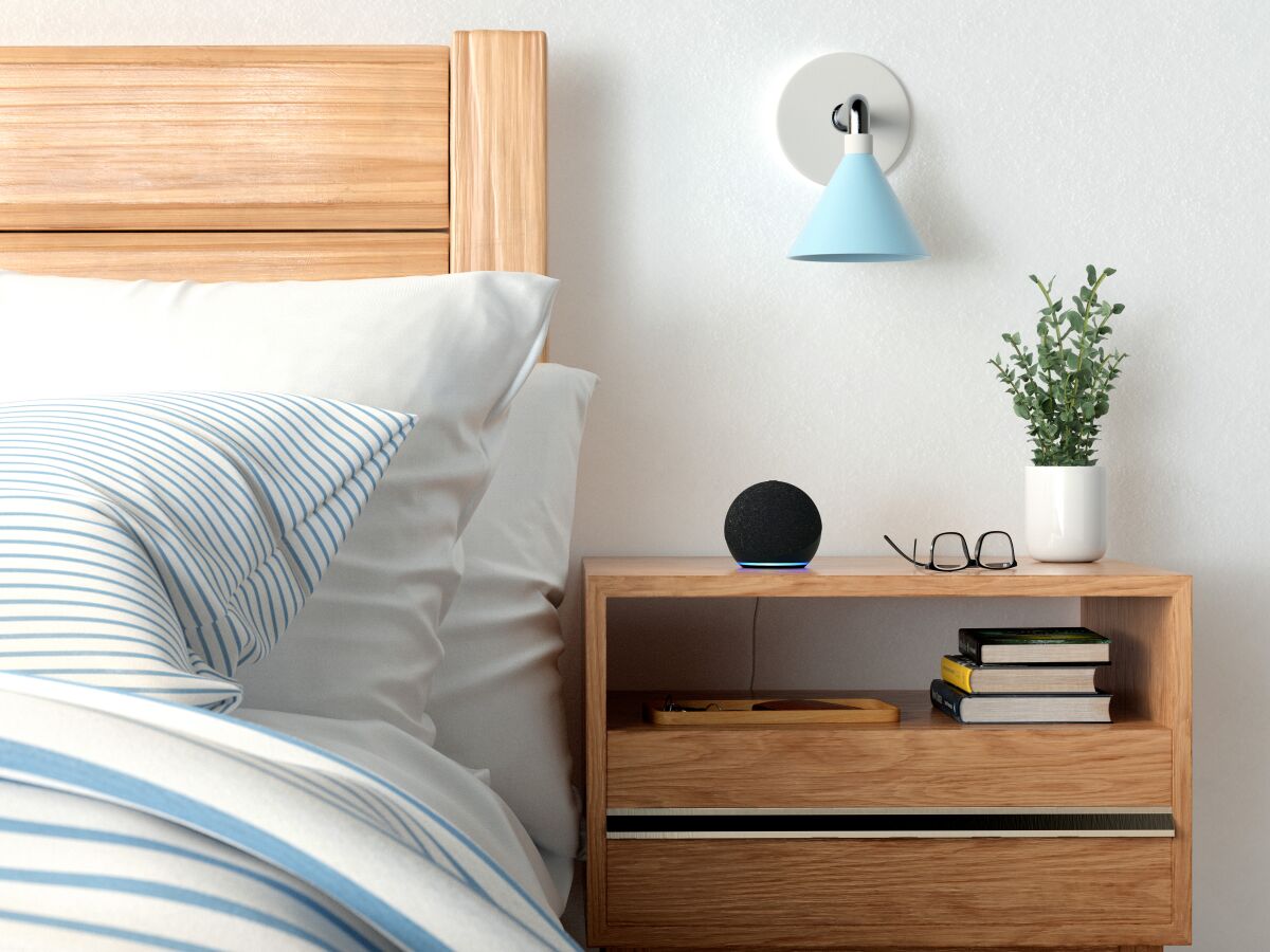 An Amazon Echo Dot sits on a bedside table.