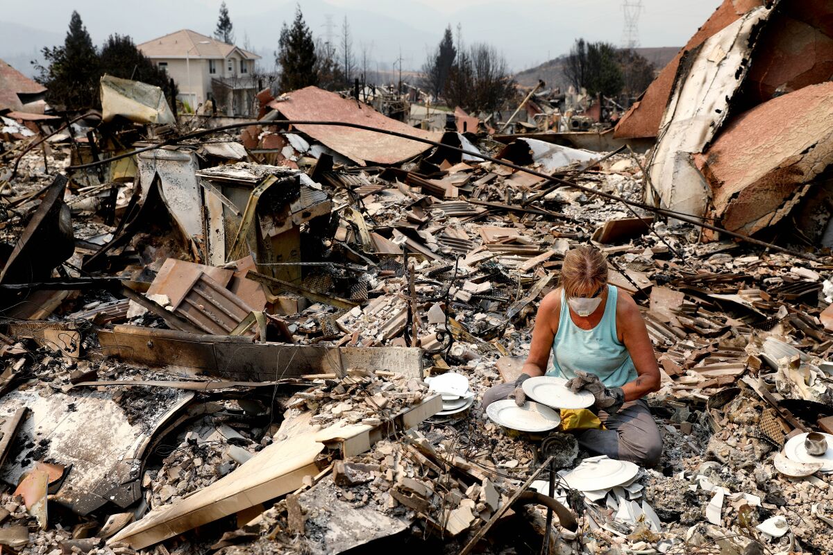 Maureen Kissick, sitting in the rubble of her home, looks through what is left of her china.