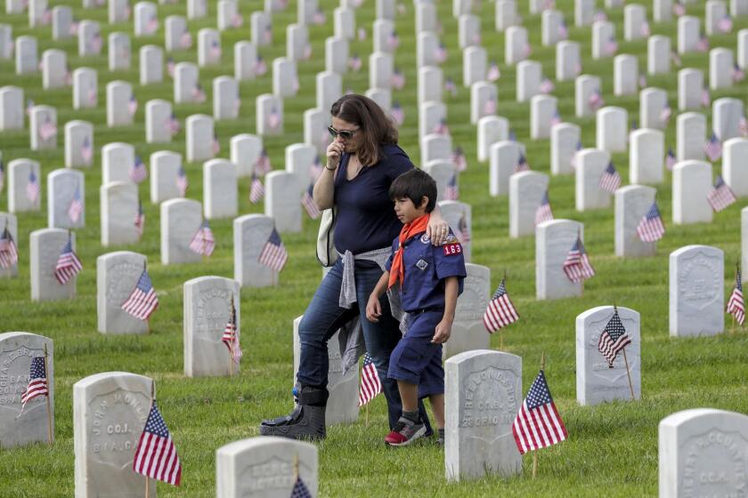 LOS ANGELES CA MAY 26, 2018 -- Jen Duffy with 6-year-old son Xavier Duffy, walks through Veteran's grave sites after placing a flag and paying her respect. More than 10,000 Scouts place 90,000 flags on Veterans' graves at Los Angeles National Cemetery to honor and remember their sacrifices on Memorial Day. (Irfan Khan / Los Angeles Times)