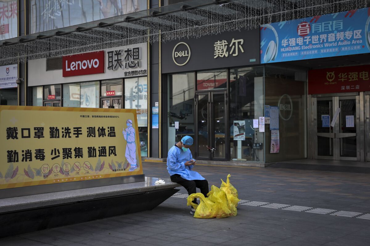 A man wearing a face mask browses his smartphone as he takes a rest on a bench displaying a coronavirus prevention poster near the shuttered shops in Huaqiangbei area, the world's biggest electronics market, in Shenzhen in south China's Guangdong province on March 14, 2022. Companies in Shenzhen, a major Chinese business center, will be allowed to reopen while efforts to contain coronavirus outbreaks progress, the government said Thursday, March 17, 2022 following a citywide shutdown that rattled financial markets. (Chinatopix Via AP)