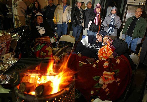 Braving an early morning chill to get a good spot to watch the 120th Rose Parade, viewers warm themselves by a small fire.