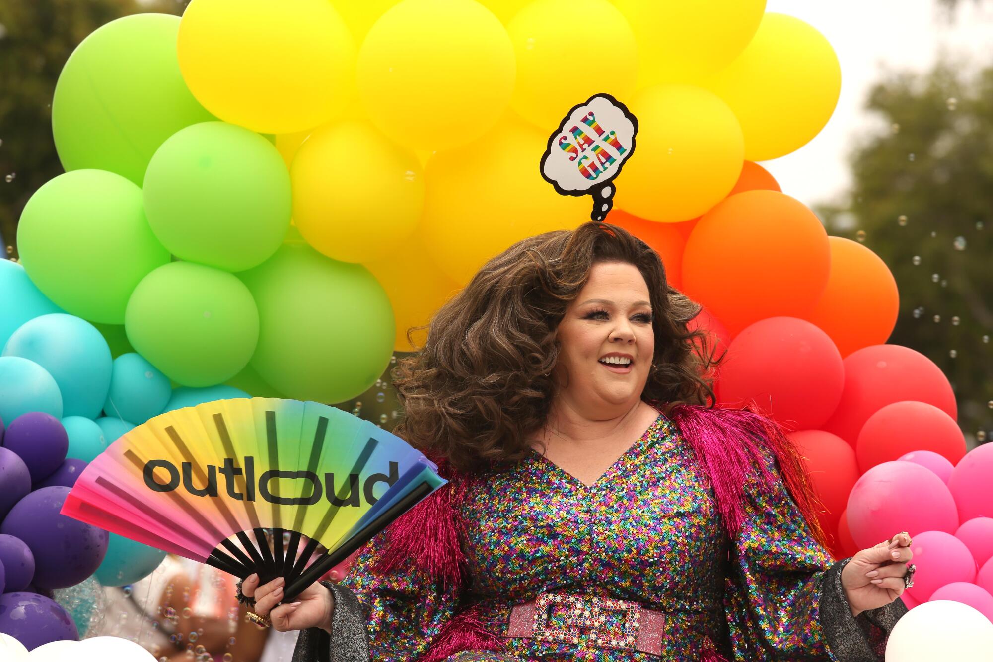 Melissa McCarthy in a sparkling gown against a backdrop of multicolored balloons.