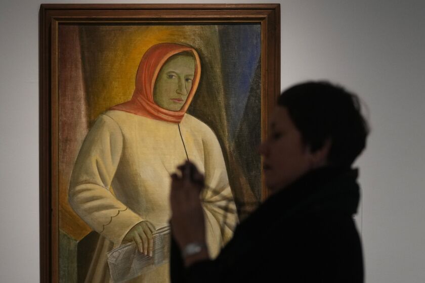 A woman takes photos next to the painting by Ukrainian artist Vasyl Sedliar called 'Portrait of Oksana Pavlenko' during the inauguration of the Ukraine art exposition at the Thyssen-Bornemisza museum in Madrid, Spain, Monday, Nov. 28, 2022. Against a backdrop of Russian attacks, border closures and a nail-biting journey across Europe, Madrid's Thyssen-Bornemisza National Museum has teamed up with Kyiv's National Art Museum of Ukraine to secretly bring dozens of Ukrainian 20th century avant garde artworks by road to the Spanish capital for a unique exhibition and statement of support for the war-torn country. (AP Photo/Paul White)