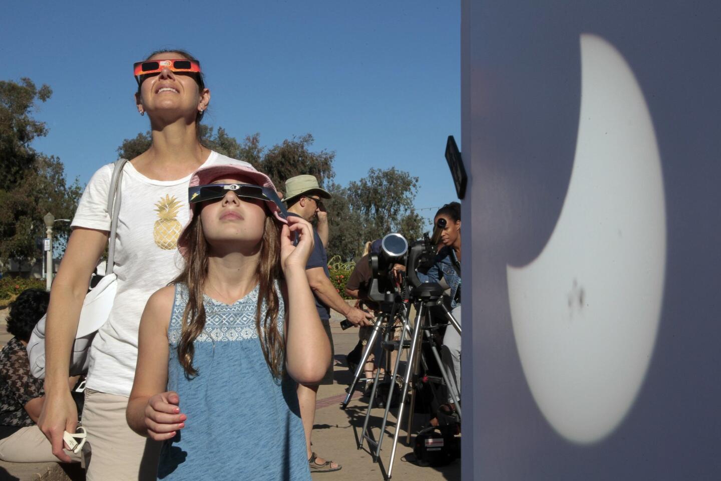 With a telescope projection of the partial solar eclipse in the foreground, Soheila Boyer and daughter Aliyeh, 8, use sun viewing glasses to look at the solar eclipse at Balboa Park on Thusday, October 23,2014.