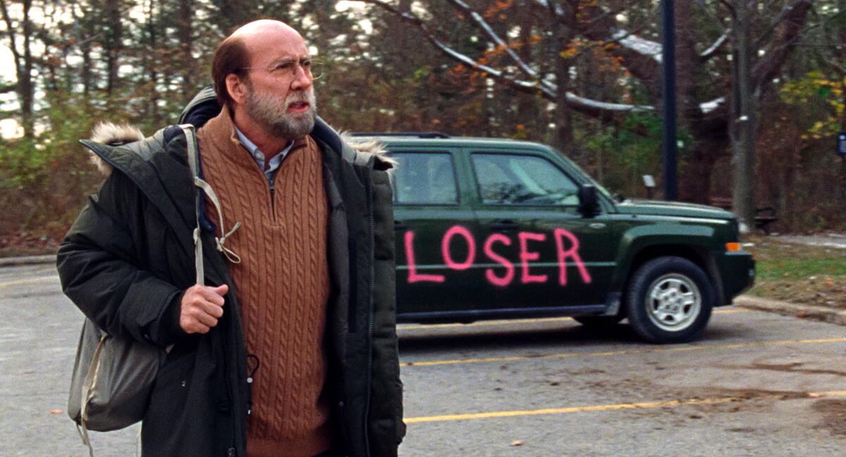 A balding, bearded, bespectacled man is upset that someone has painted "Loser" on the side of his car.