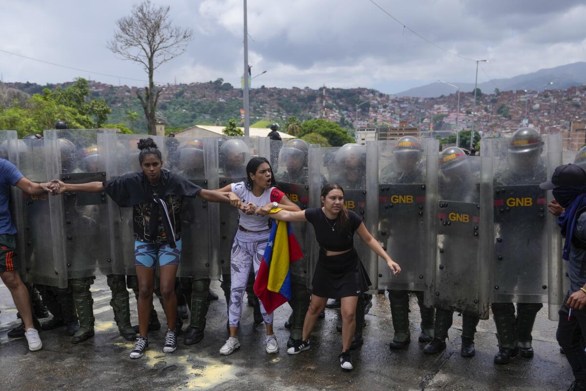 Protesters stand with their backs against riot guards' shields. 