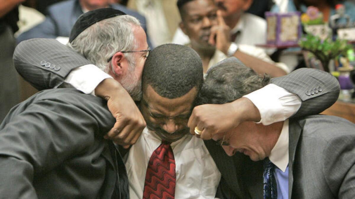 El abogado Michael Schwartz, a la izquierda, es abrazado por el ex oficial John Webb Jr., mientras también abraza al abogado William J. Hadden. Webb fue absuelto en la balacera en contra de un oficial de la fuerza aérea fuera de servicio, en el 2007.