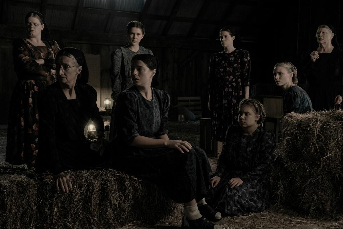 Eight women dressed in Mennonite clothing in a dimly lighted hayloft.