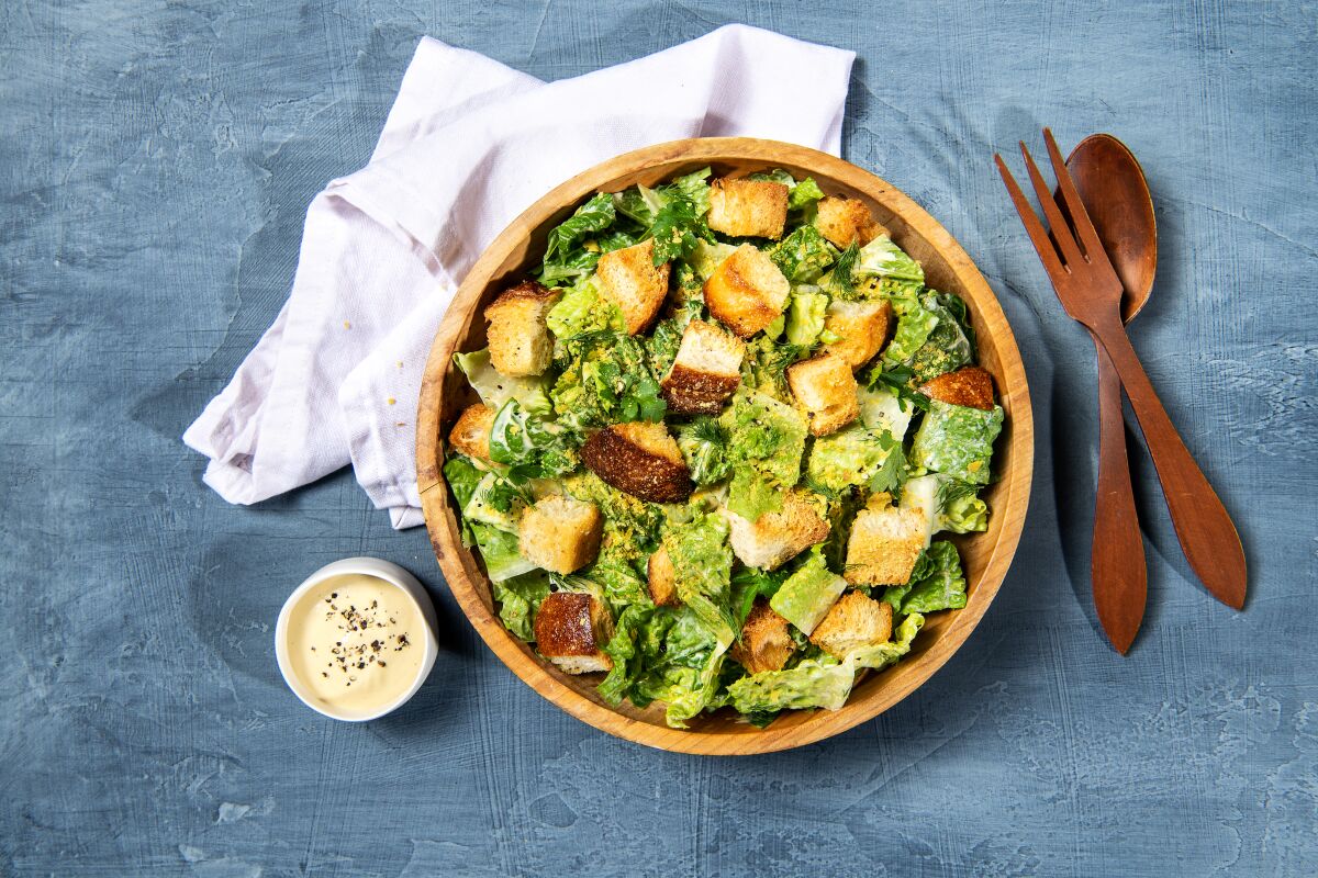 Lodge Vegan Caesar Salad in una ciotola di legno con una forchetta e un cucchiaio di legno e una tazza di condimento
