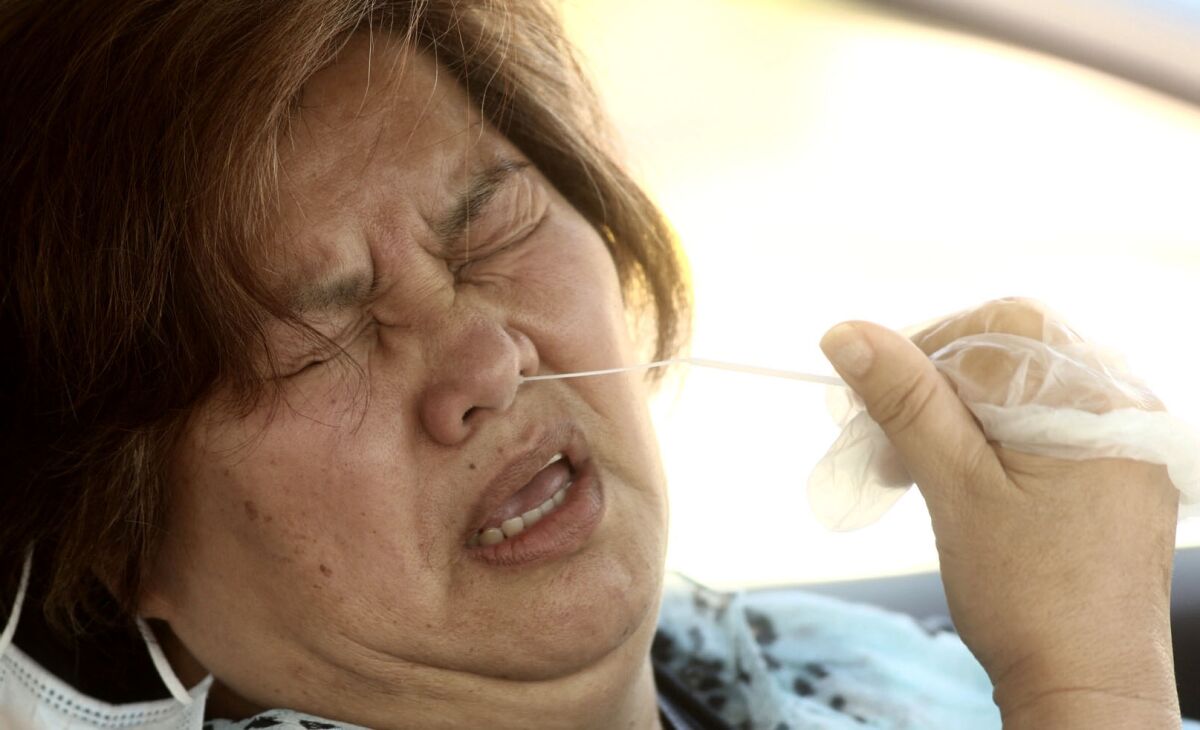 A Carson resident grimaces as she gives herself a coronavirus test with a swab in her nostril while sitting.
