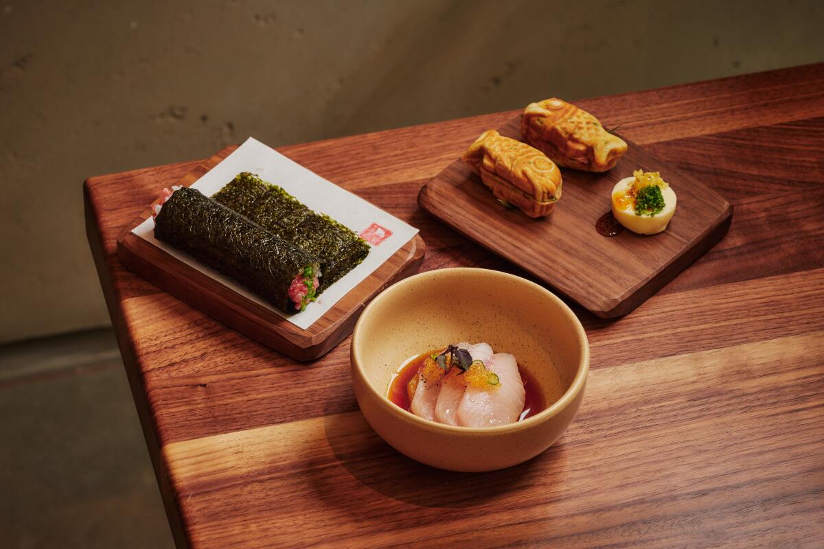 A trio of Uchi dishes on wood table: hand roll, sashimi and taiyaki.