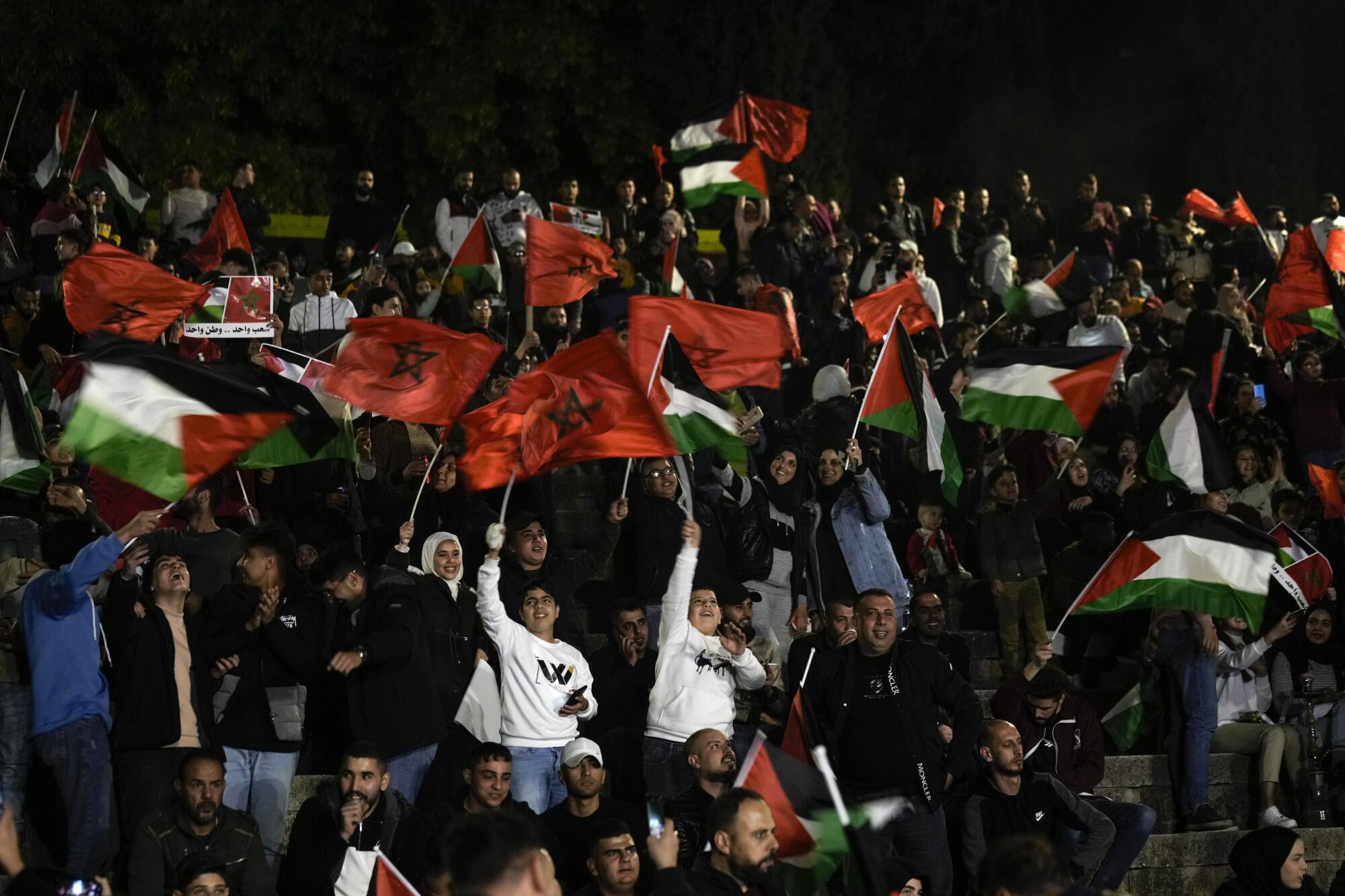 Palestinians in the West Bank town of Nablus wave Moroccan and Palestinian flags as they watch Morocco play Portugal