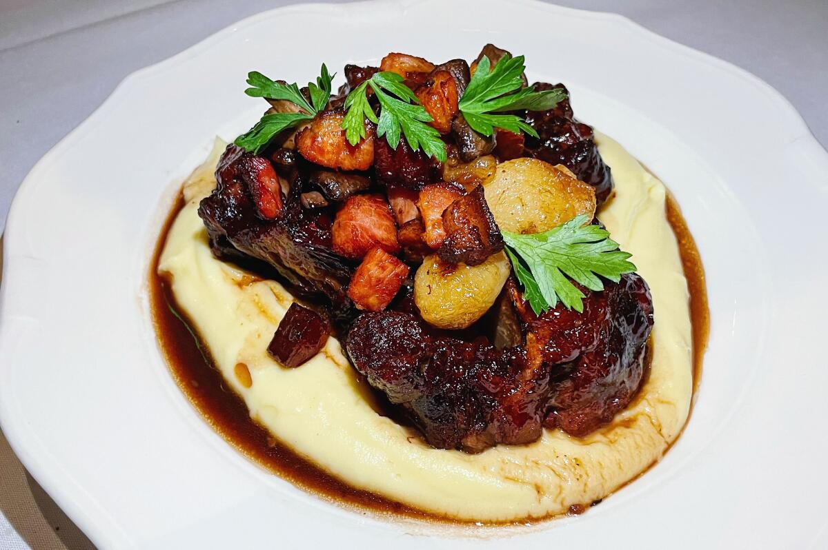 Three oxtail served bourguignon-style atop mashed potatoes on a white plate 