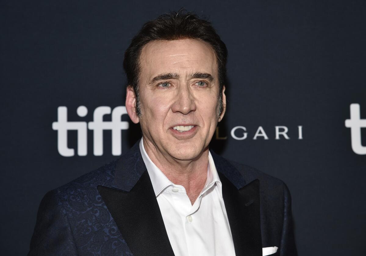 Nicolas Cage wears a black suit and white collared shirt as he poses for photos