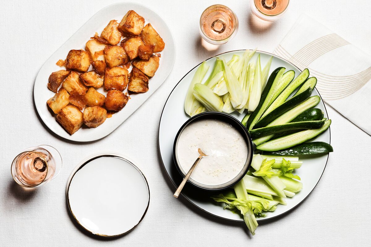 Fried Potatoes on a plate next to a plate of sliced vegetables with a small bowl of a white dip