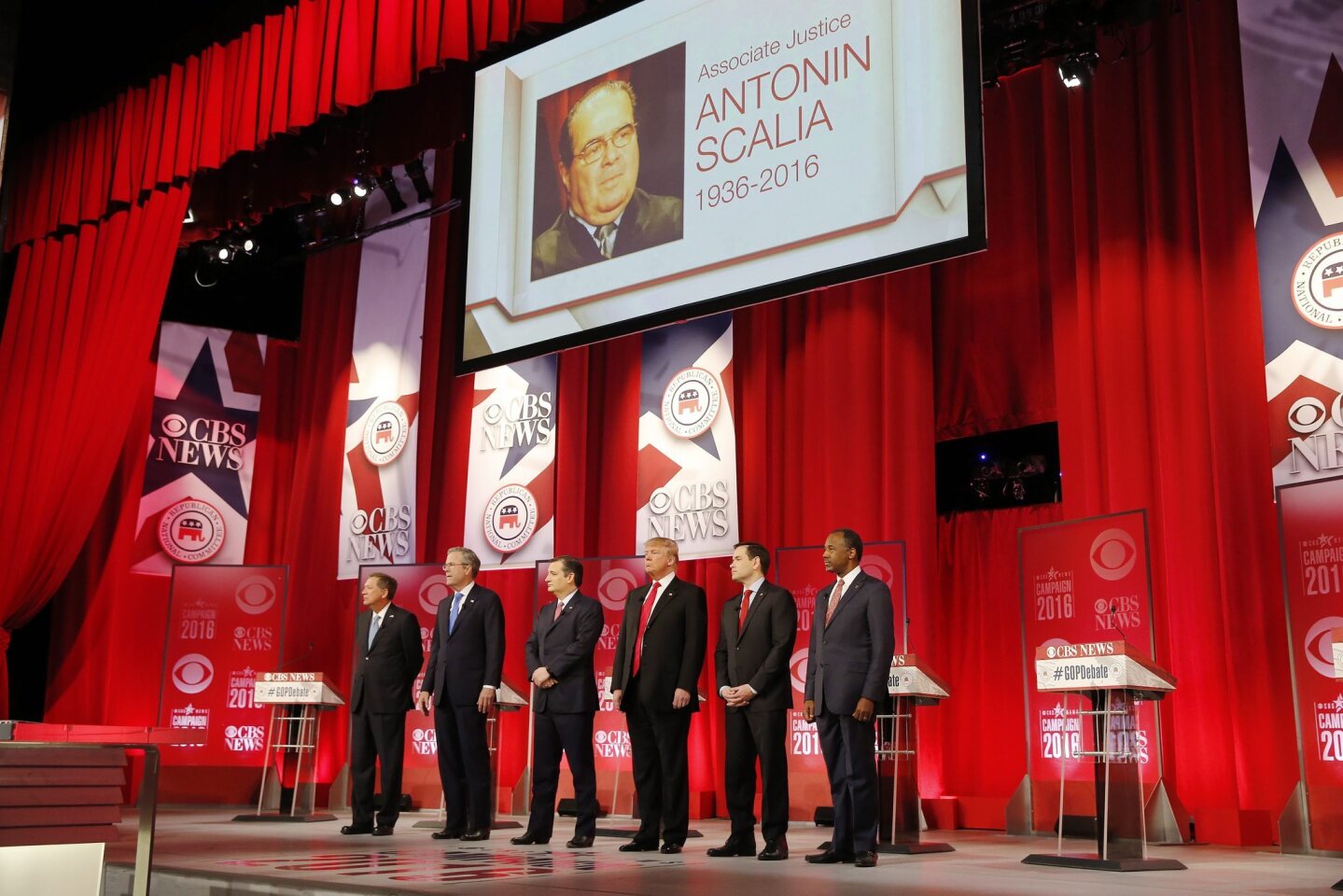 John Kasich, Jeb Bush, Ted Cruz, Donald Trump, Marco Rubio and Ben Carson take the stage beneath an image of U.S. Supreme Court Justice Antonin Scalia, who died earlier in the day.