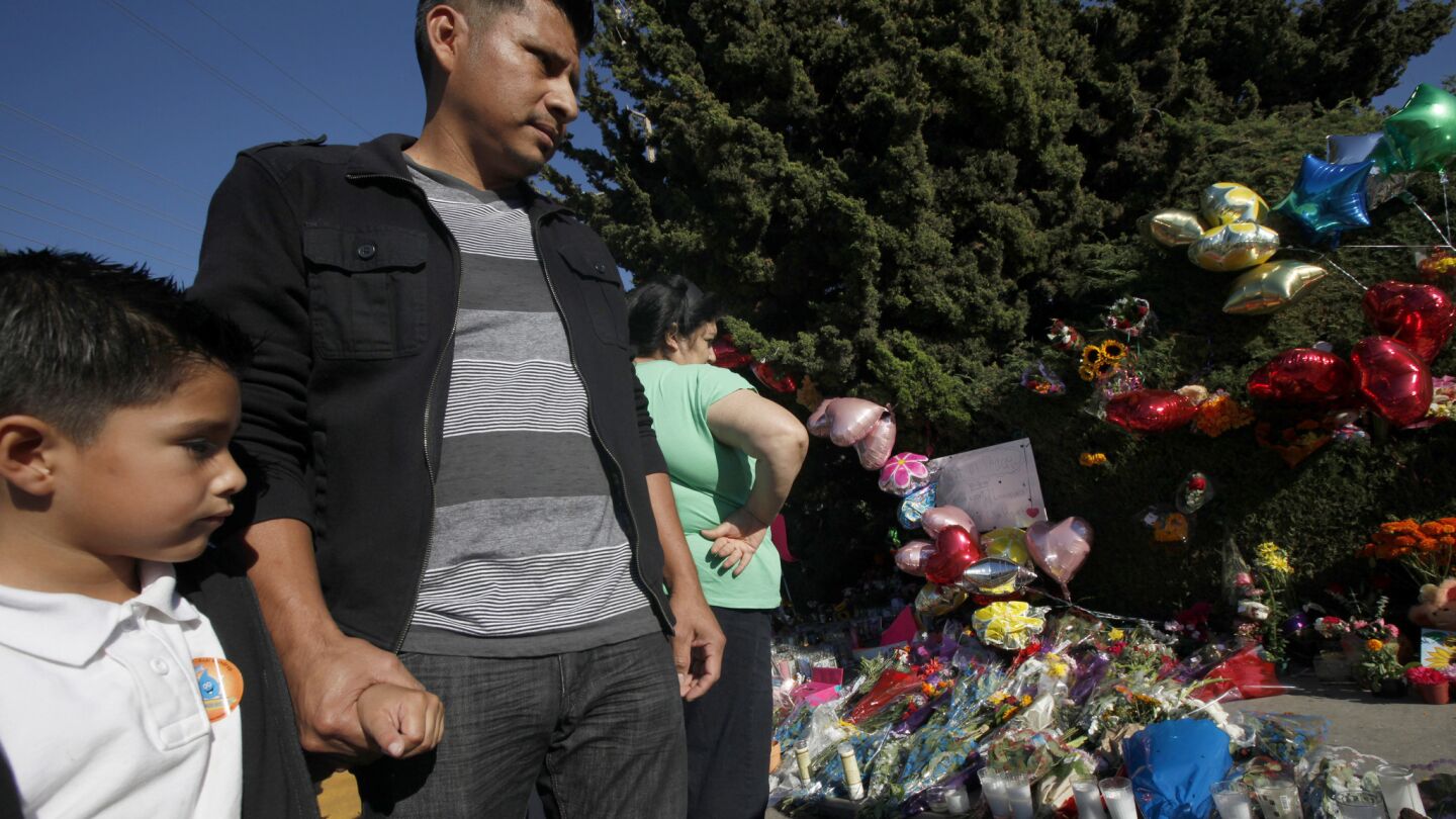 Amilio Cortez holds on to his son Brandon, 5, a kindergarten student at Fairview Elementary School, as they walk past the memorial for the three teenage girls who were killed Halloween night by a hit-and-run motorist.