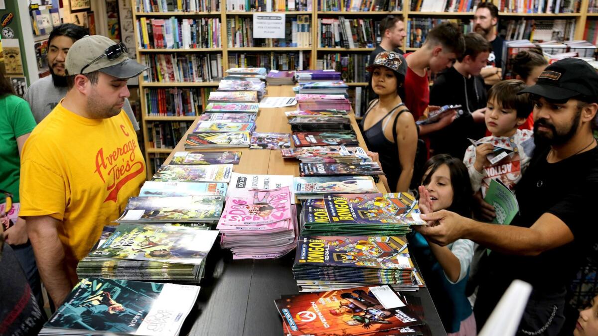 Customers look over a stack of free comics at House of Secrets Comics and Toys in Burbank during last year's Free Comic Book Day event.