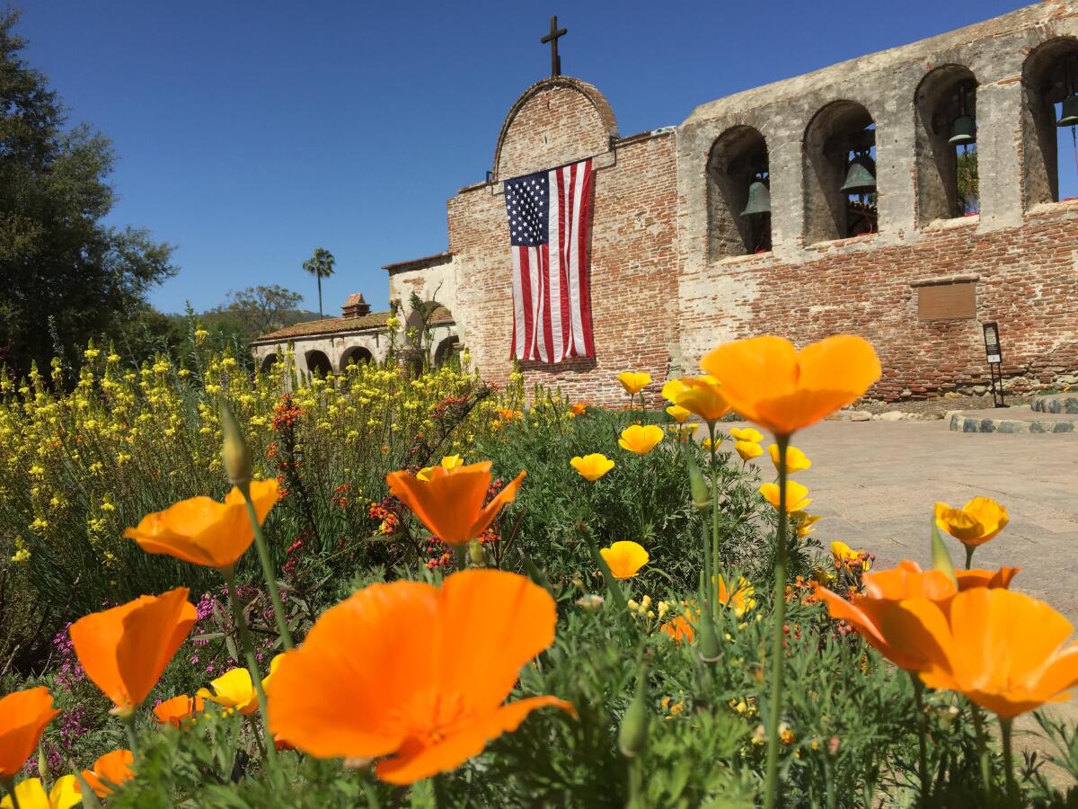Mission San Juan Capistrano with a U.S. flag and California poppies.
