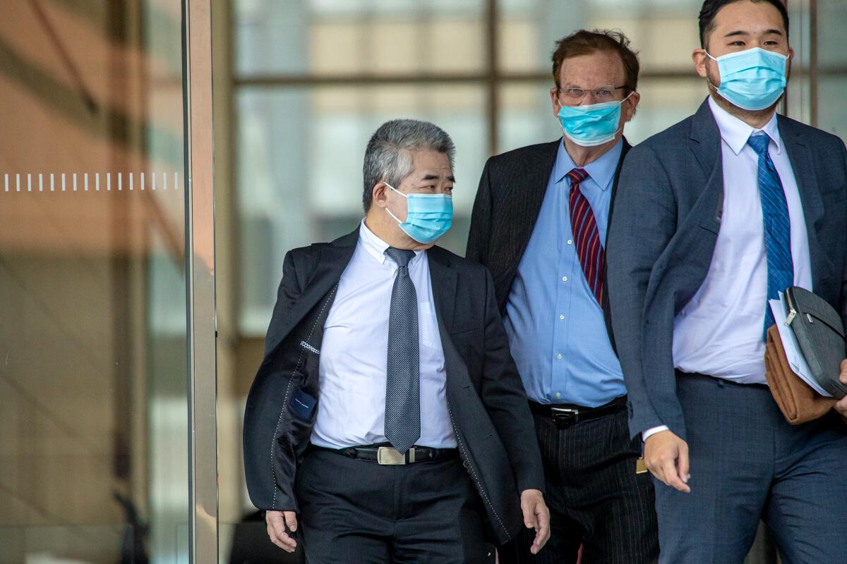 Three men wearing suits and surgical masks near glass doors of a courthouse