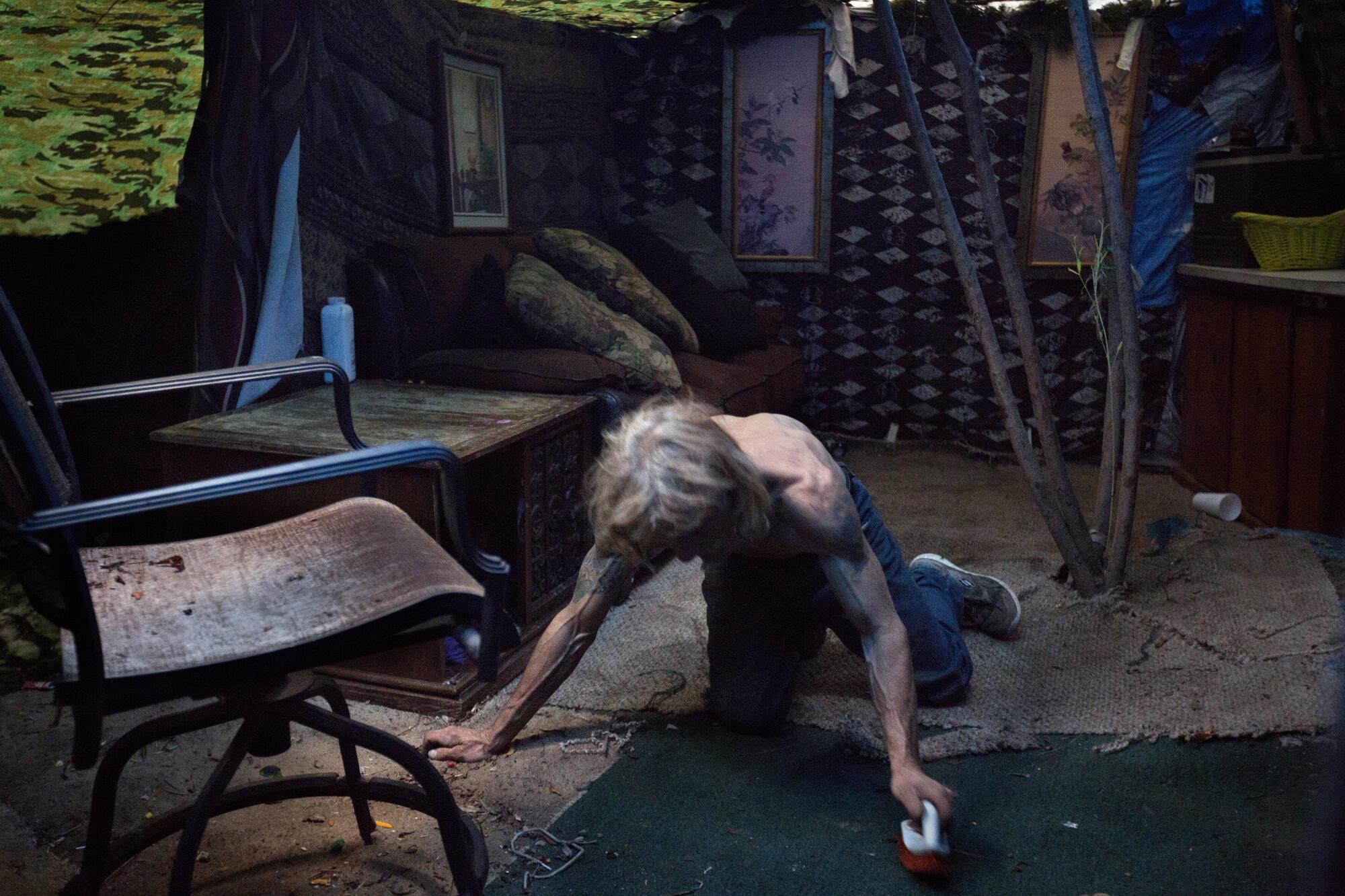 Alan Fagerson, 54, cleans the floor of his home, which is made of wood and found materials.