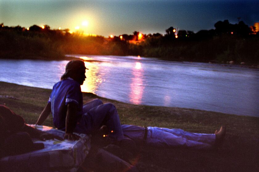 Young Honduran migrants rest on the Mexican side of the Rio Grande. In the distance, U.S. Border Patrol lights illuminate Zacate Creek in Texas.