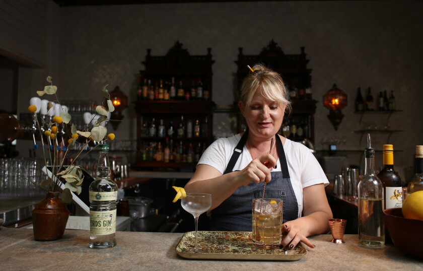 A woman at a bar counter mixes a drink that sits on a tray.