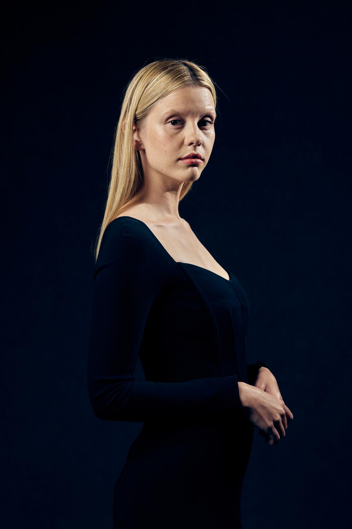 A woman with long blond hair poses in a black outfit.