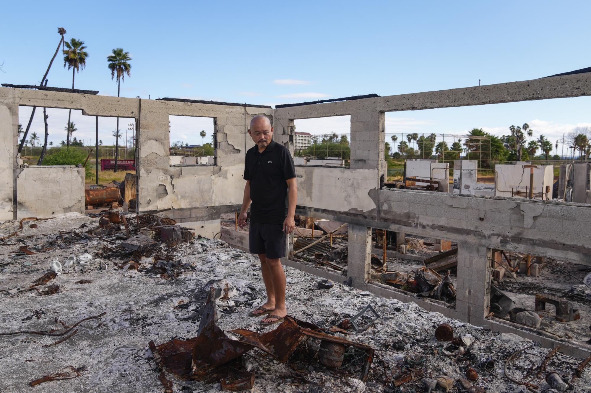 The Rev. Ai Hironaka stands amid the charred remains of a building. 