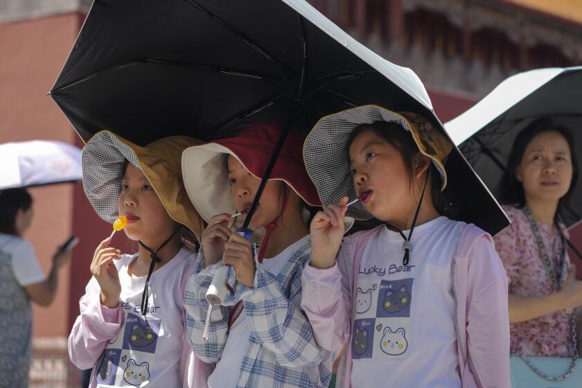 Children wearing sun hats and carrying an umbrella pose for a souvenir photo near the Forbidden City on a sweltering day in Beijing, Friday, July 7, 2023. Earth's average temperature set a new unofficial record high on Thursday, the third such milestone in a week that already rated as the hottest on record. (AP Photo/Andy Wong)