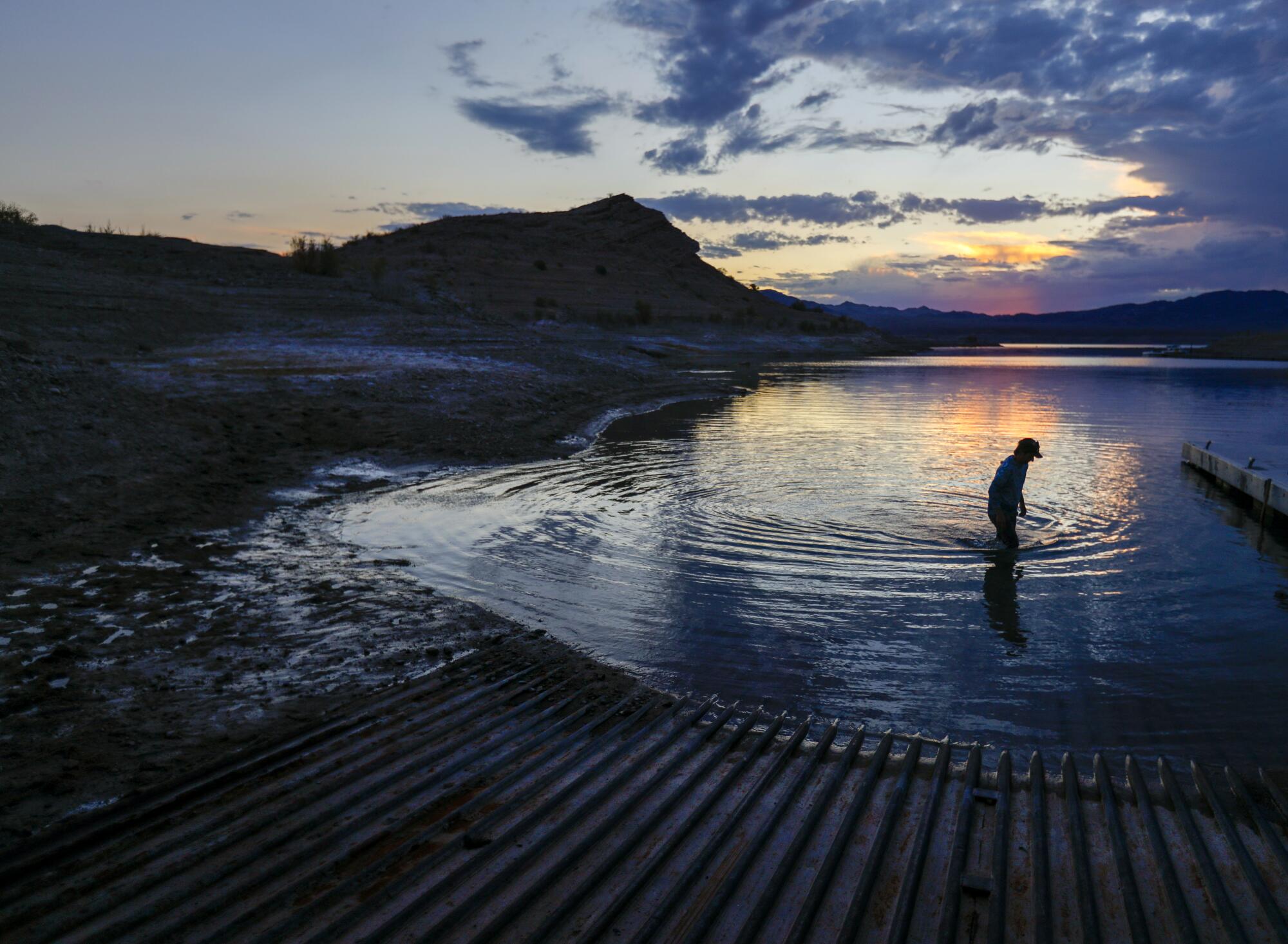 A man wades in shallow water at sunset