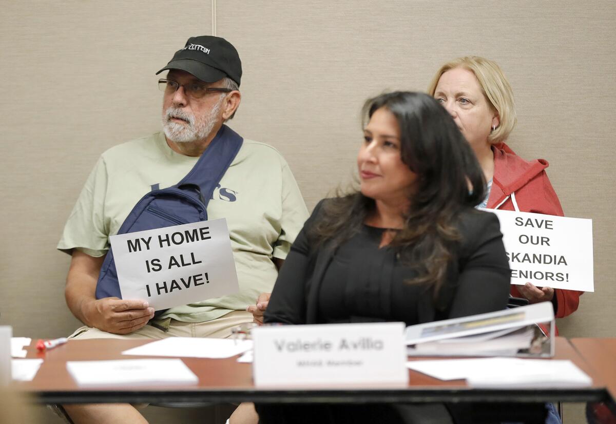 Mobile home residents hold signs behind board member Valerie Avilla during Monday's meeting.