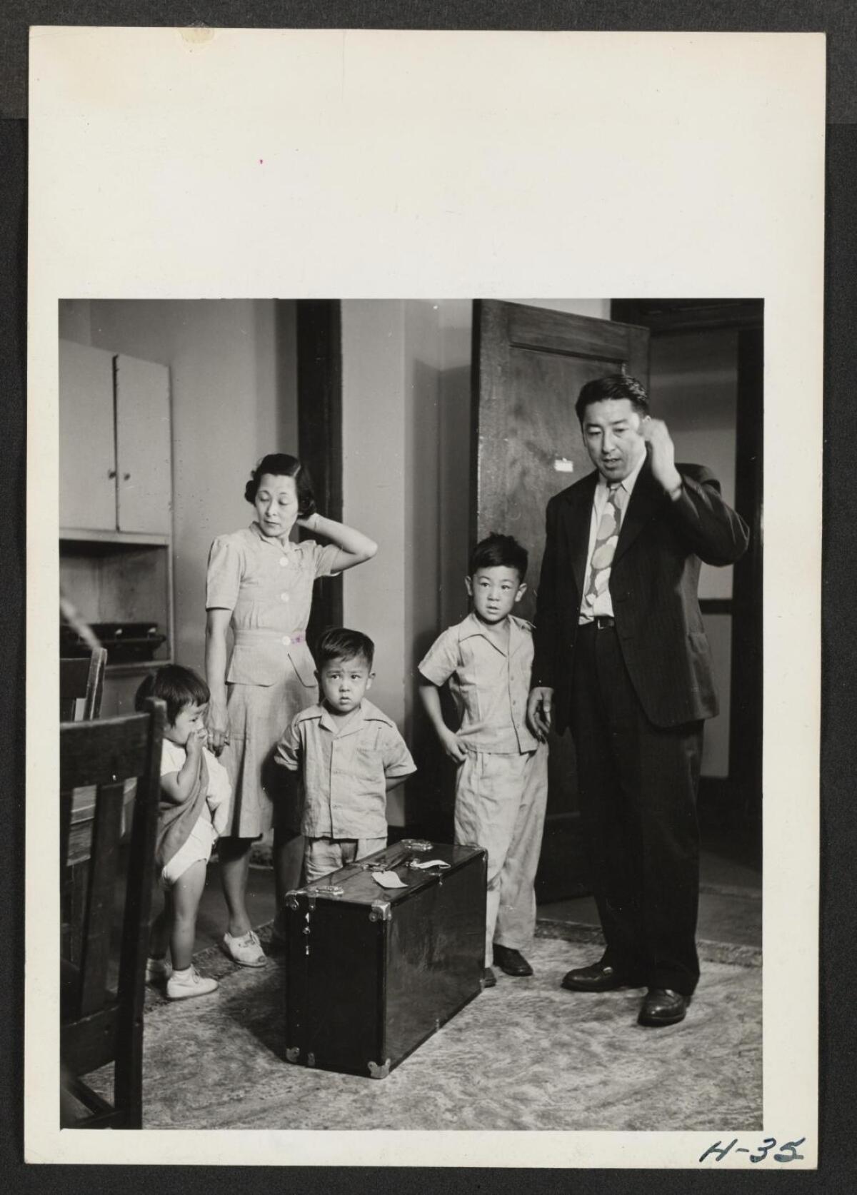A black-and-white photo of two parents and three small children and a suitcase 