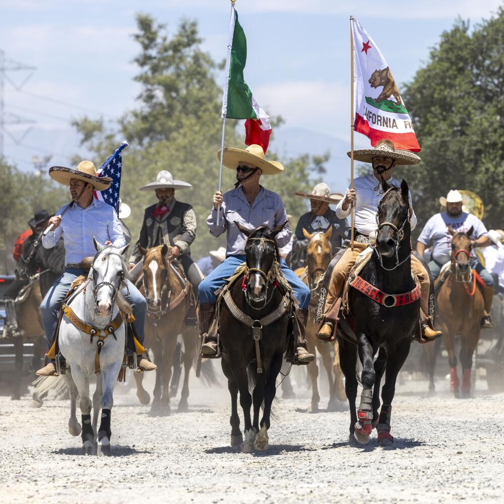 People in sombreros while on horseback hold flags